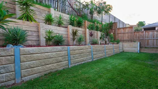 A beautifully landscaped backyard showcasing multi-level retaining walls made of stone blocks, adorned with lush greenery and a vibrant lawn.