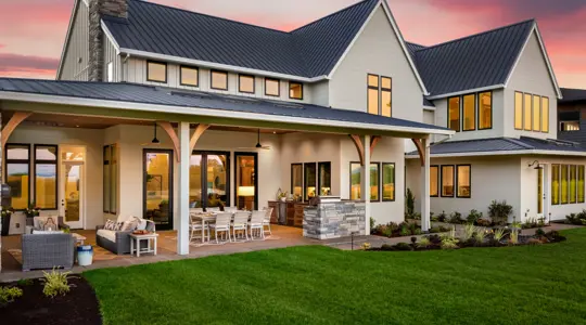 A beautiful modern farmhouse home with a large, inviting patio and lush green lawn under a sunset sky, perfect for residential landscaping projects.