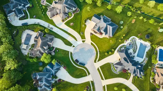 An aerial view of a beautifully landscaped luxury neighborhood with large homes, green lawns, and winding drives, showcasing exceptional curb appeal.